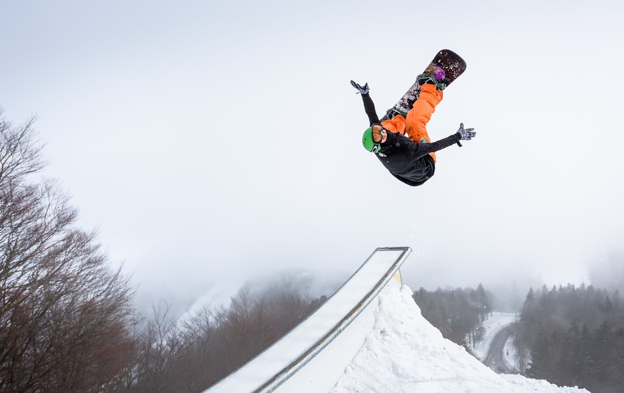 A snowboarder upside down in the air above a snow jump