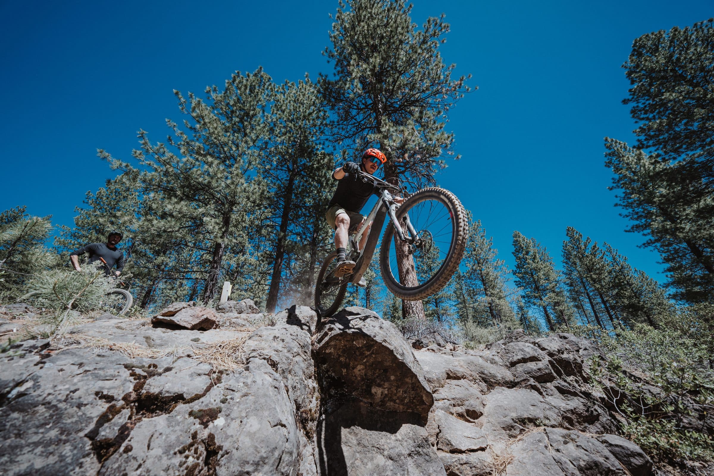 Mountain biker riding over a rock among ponderosa pines, Bend, Oregon, blue sky