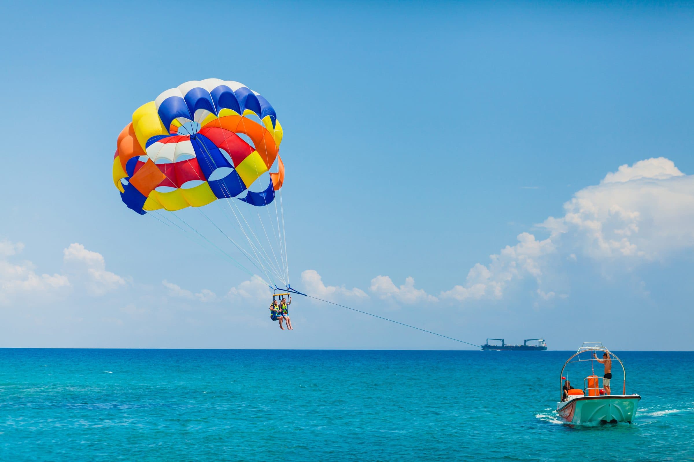 Parasailers under a rainbow canopy with the tow boat over emerald Destin water