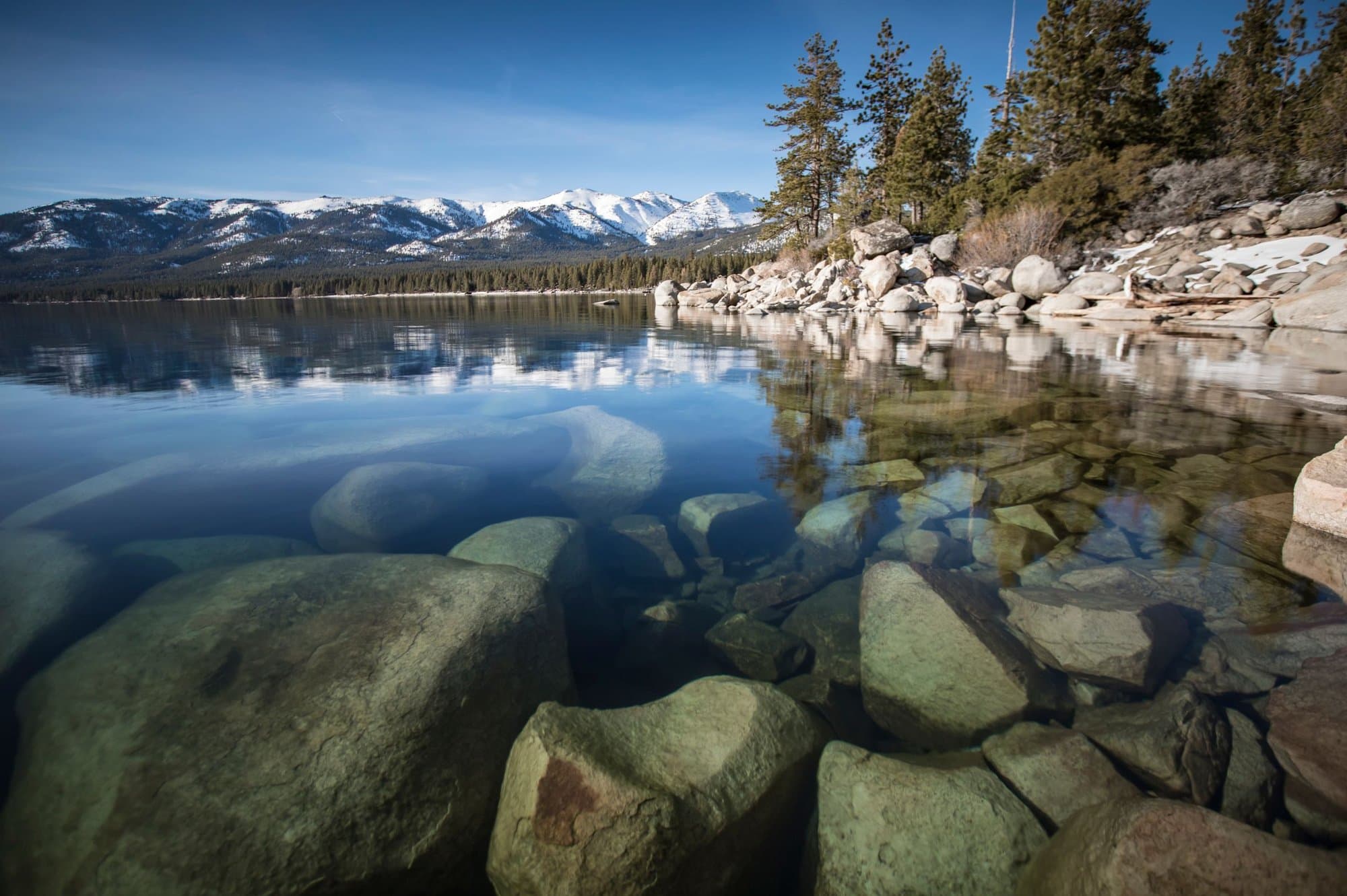 Clear Lake Tahoe water with rocky shoreline and snowy mountains