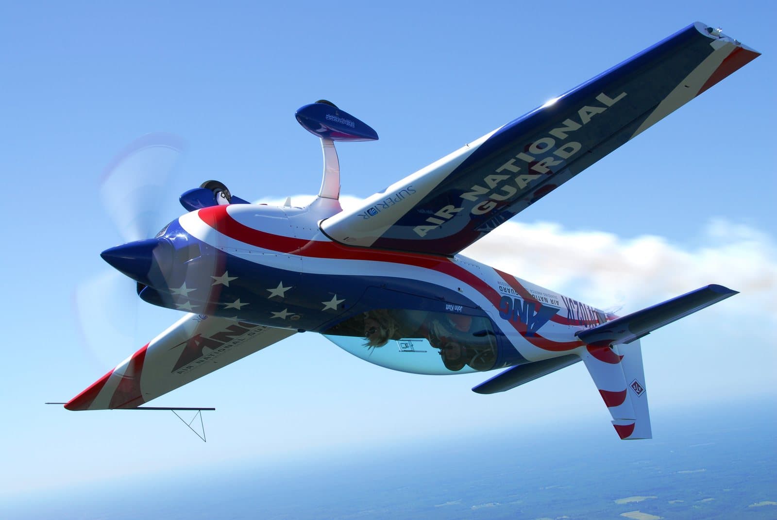 A red, white, and blue stunt plane flying inverted against a blue sky