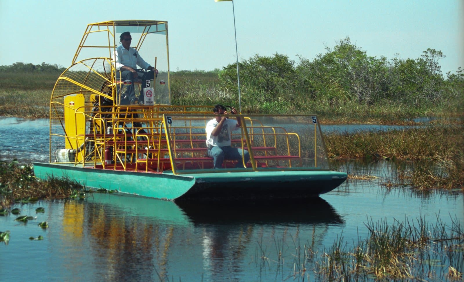 An airboat with a large rear fan carrying passengers through Everglades marsh