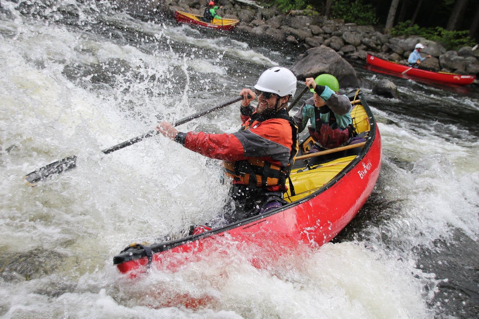 Two paddlers in helmets turning a red tandem canoe through whitewater