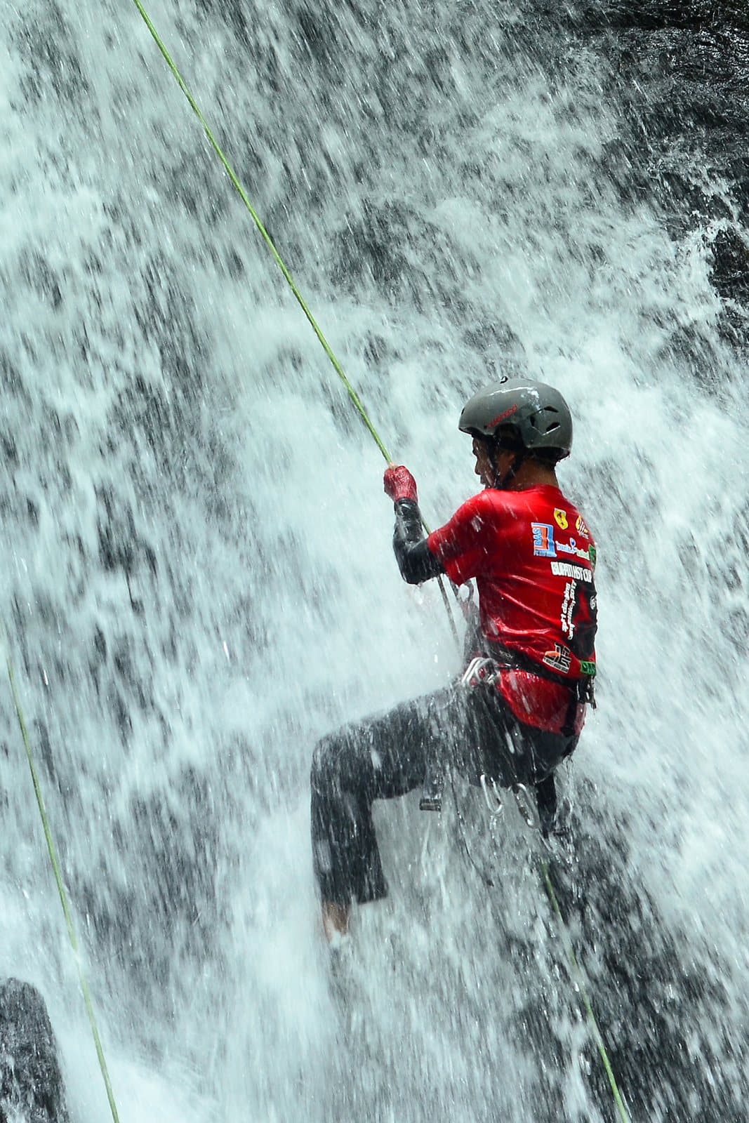 A canyoneer in a helmet rappelling down through a waterfall