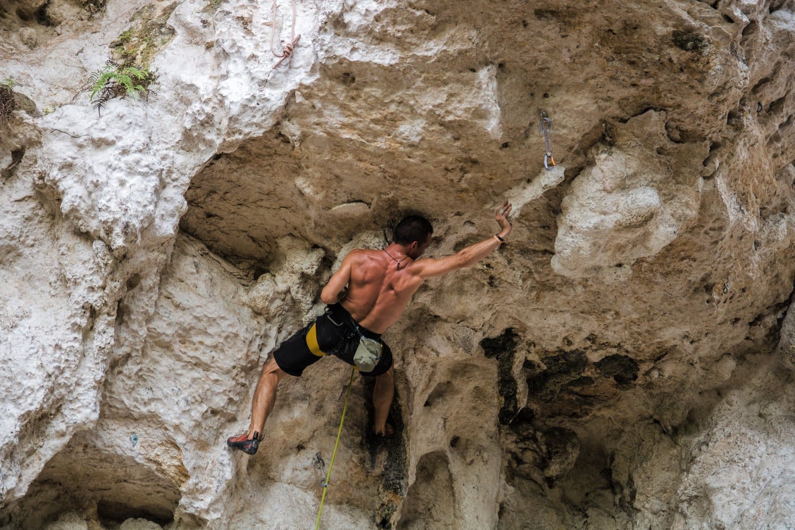 A sport climber reaching for a hold on an overhanging limestone wall