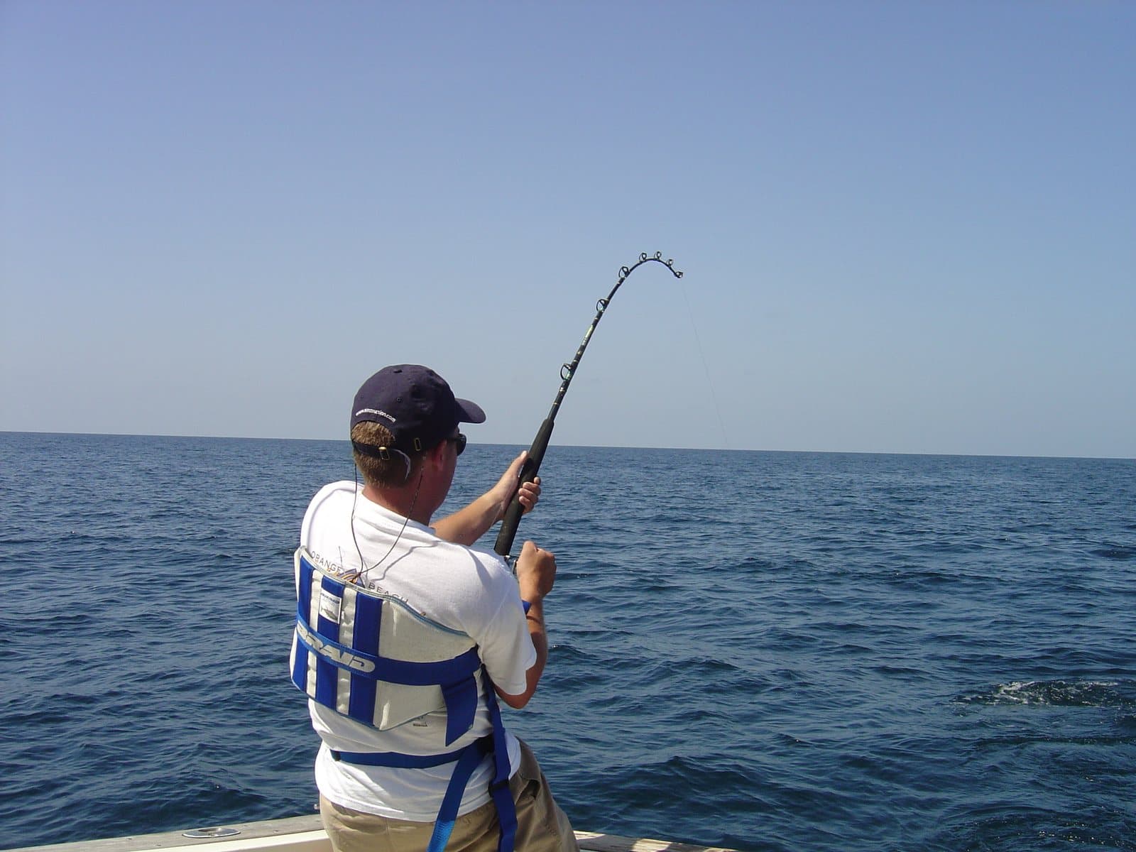 An angler fighting a fish with a bent rod from a boat on the open ocean