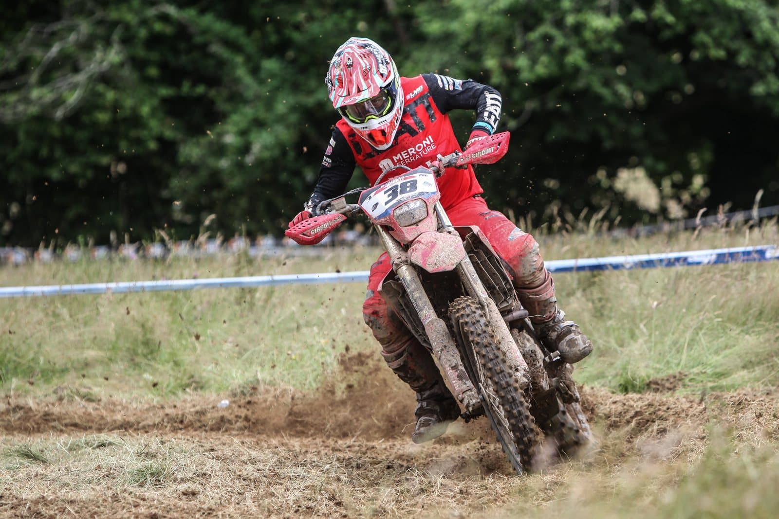 An enduro dirt bike rider cornering through dirt and grass