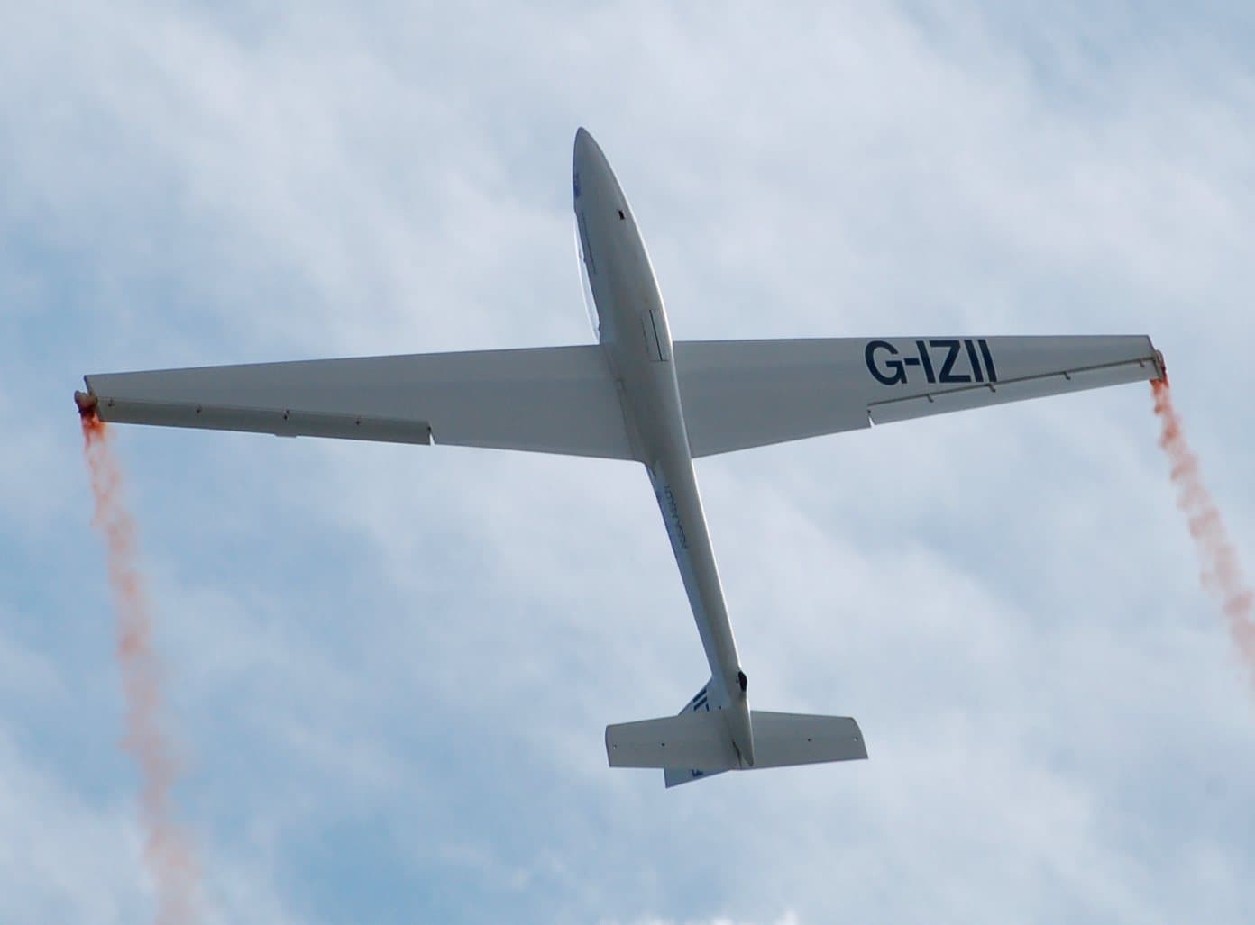 A white sailplane flying overhead with smoke trailing from both wingtips