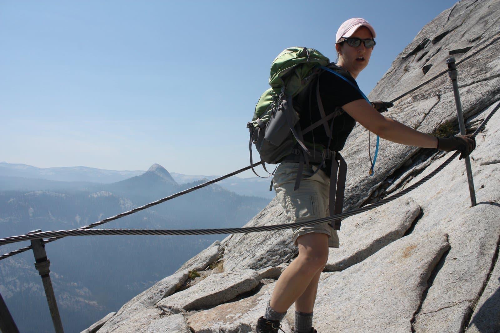 A hiker holding the cables on a steep granite climb above a valley