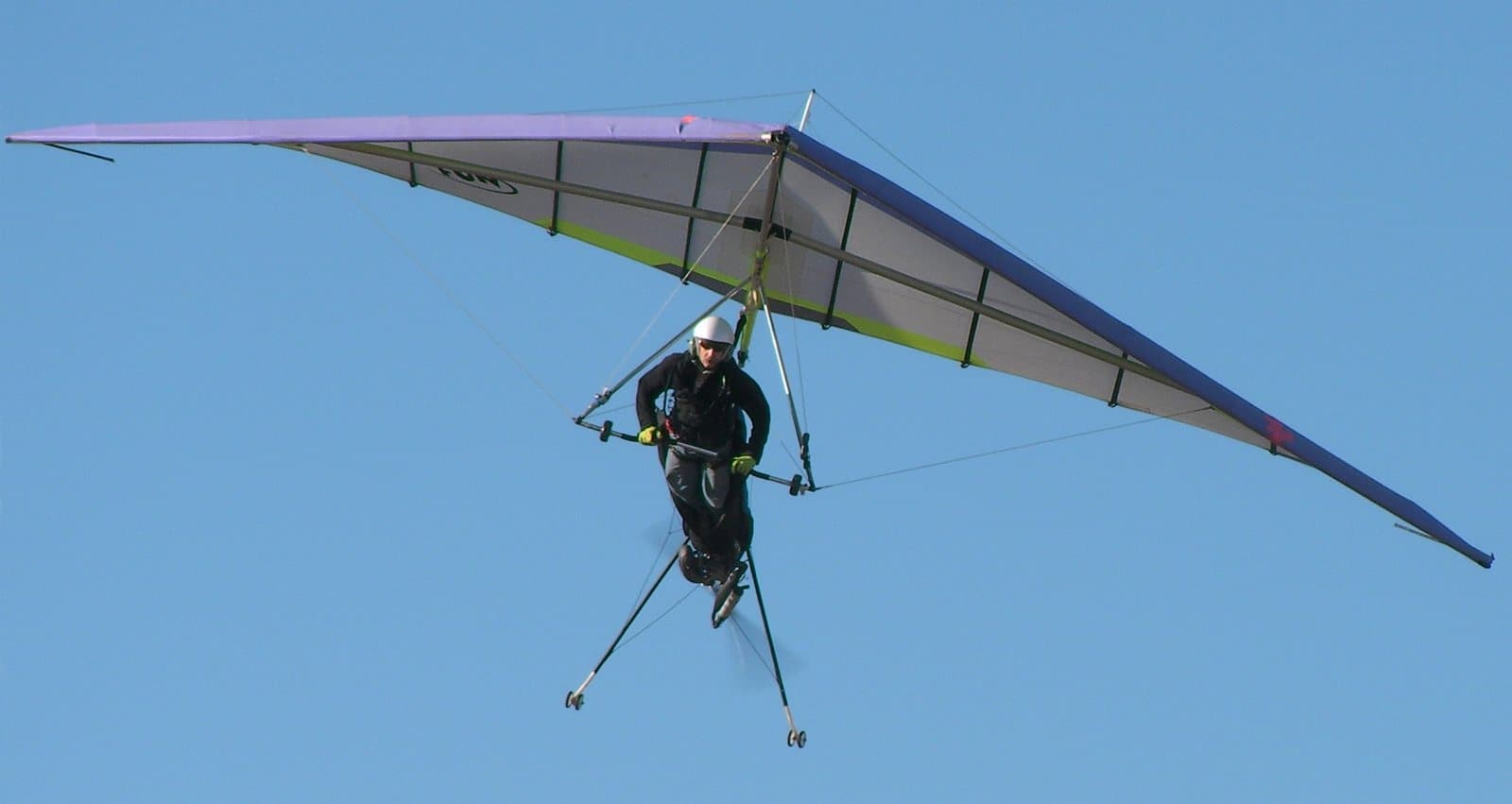 A pilot flying a hang glider against a clear blue sky