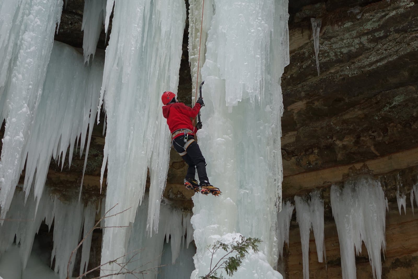 An ice climber with axes and crampons on a frozen waterfall