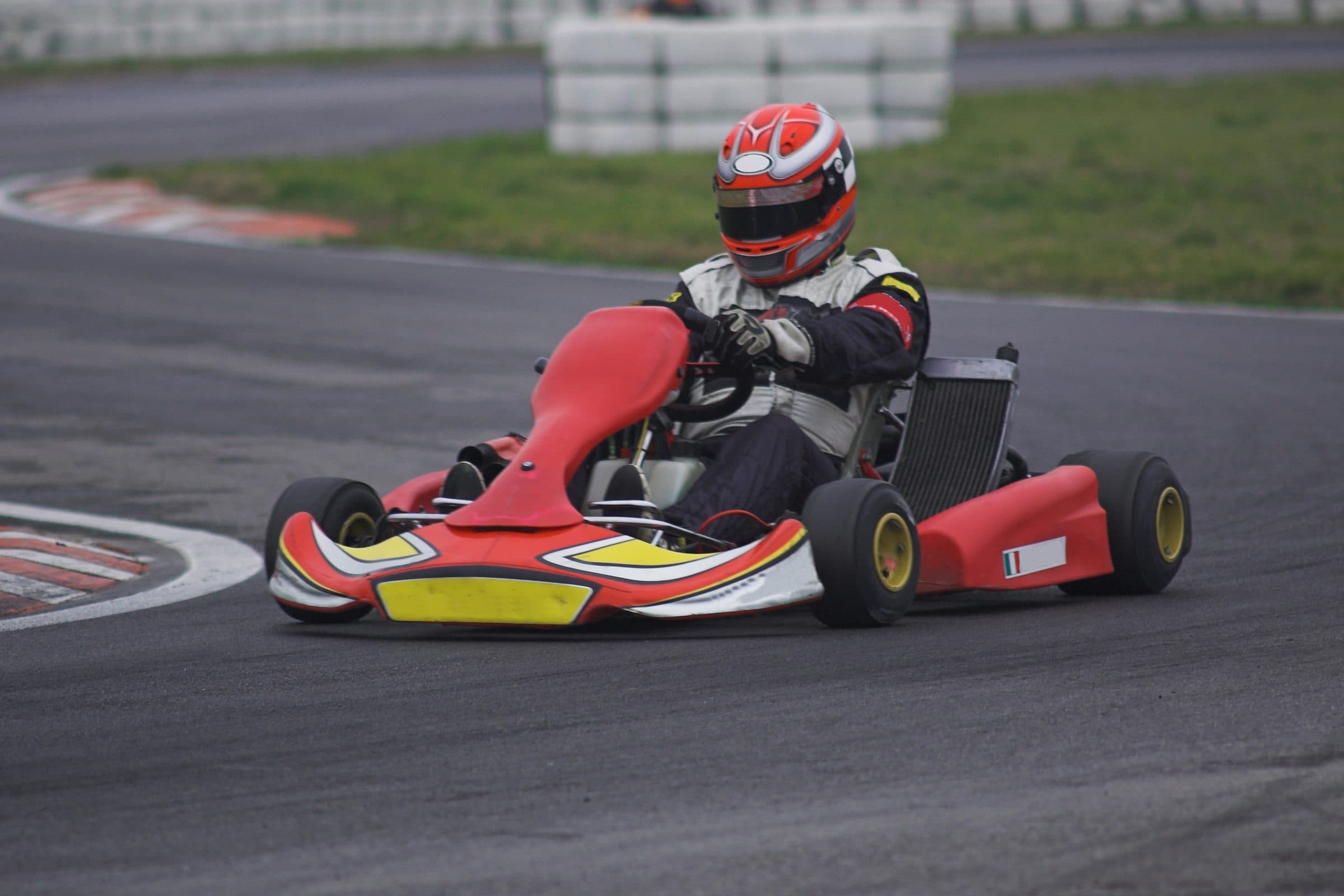 Kart racer in a race suit leaning into a corner on an outdoor track