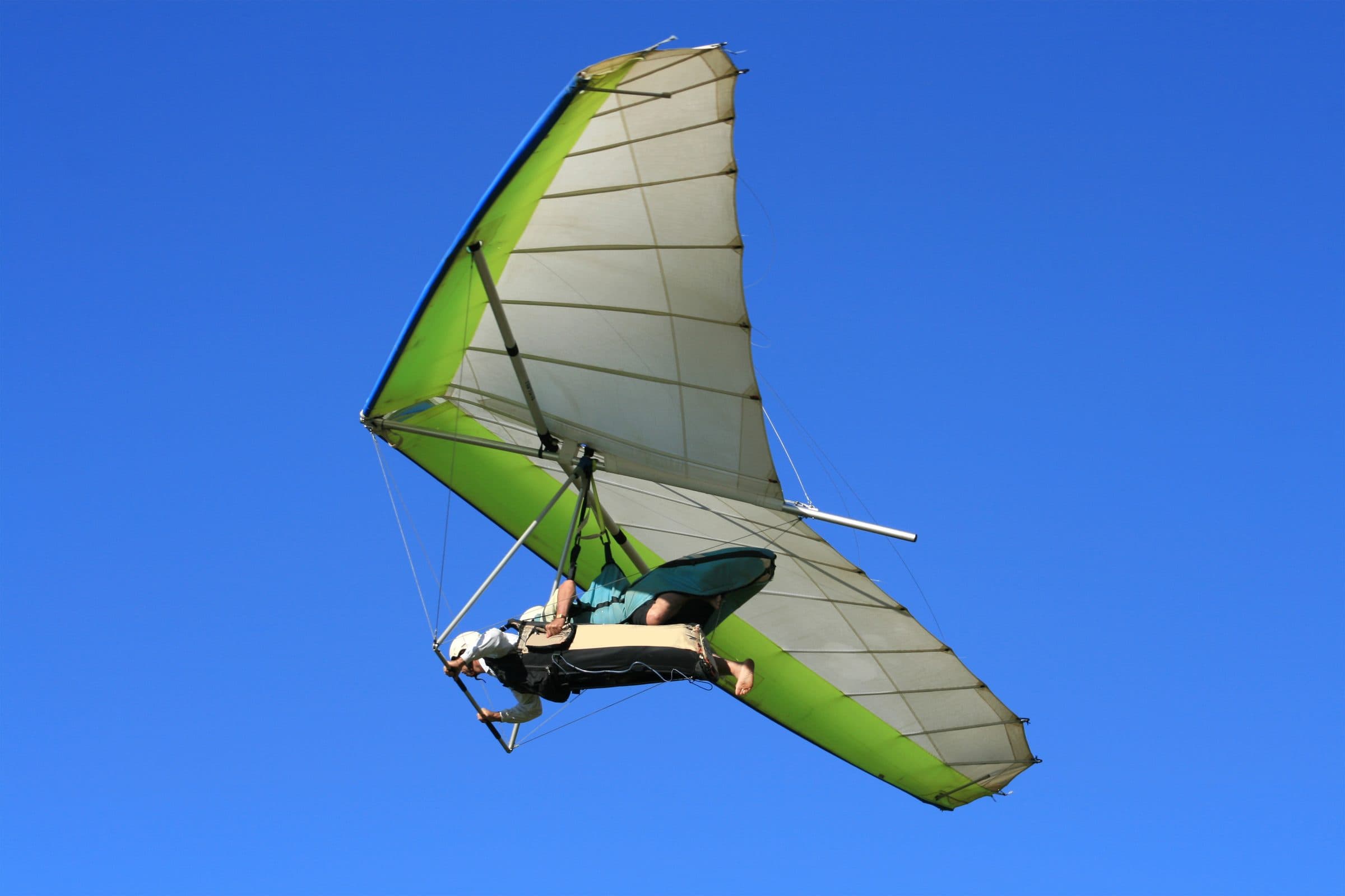 Hang glider pilot flying a green wing against a deep blue sky