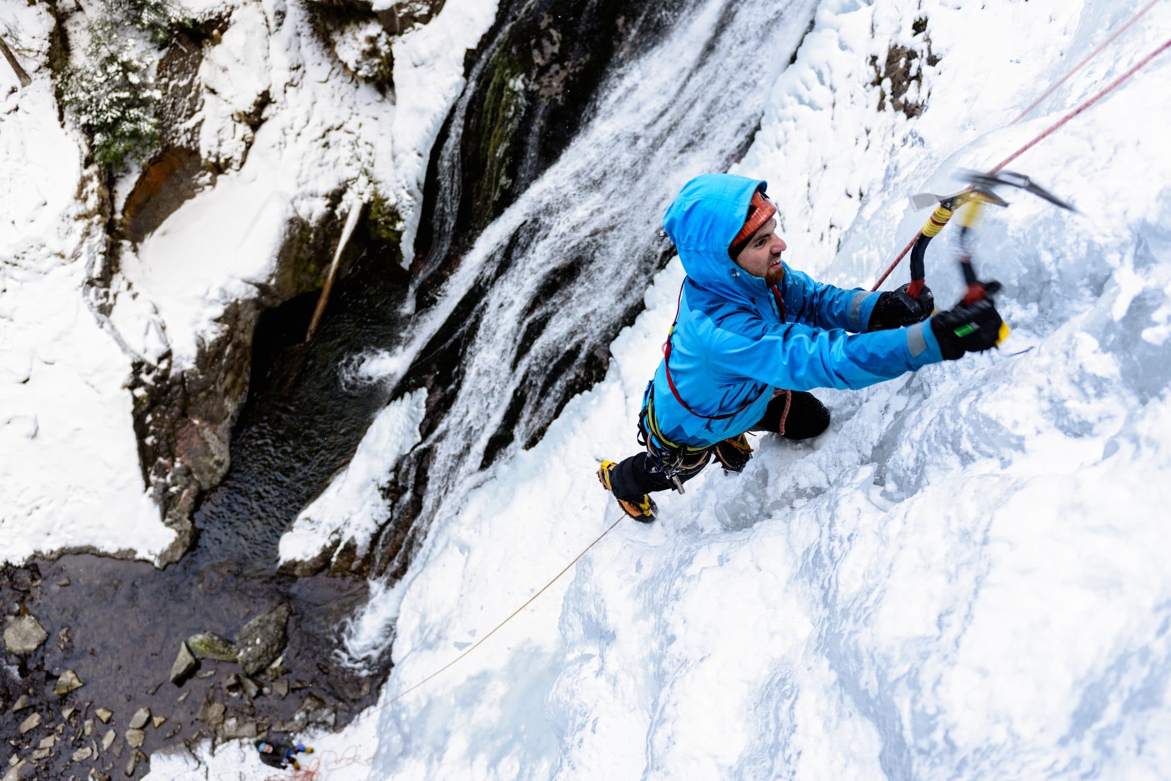 Ice climber in blue swinging axes on a frozen waterfall