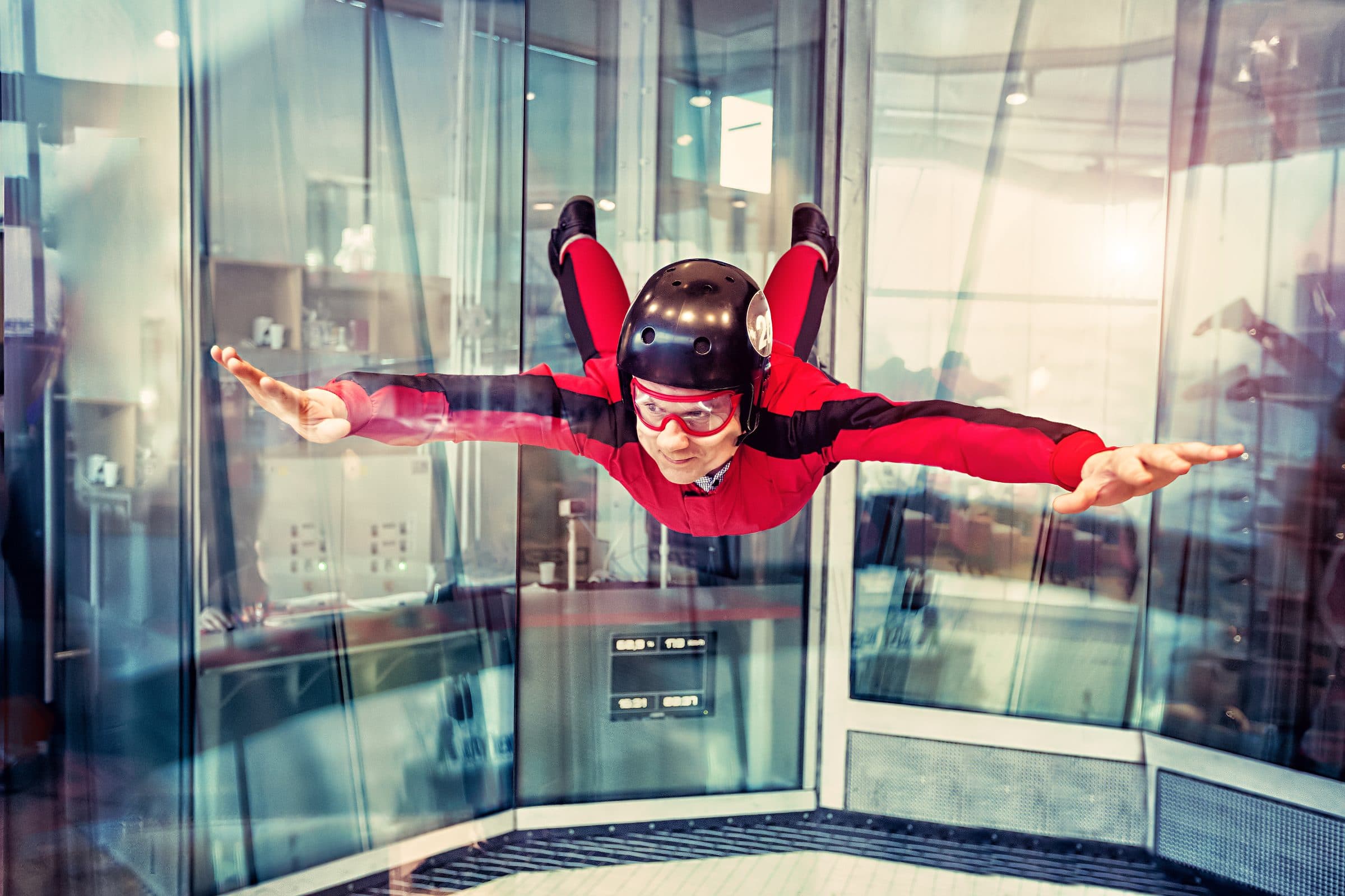 Flyer in a red suit bodyflying in a glass wind tunnel, face visible