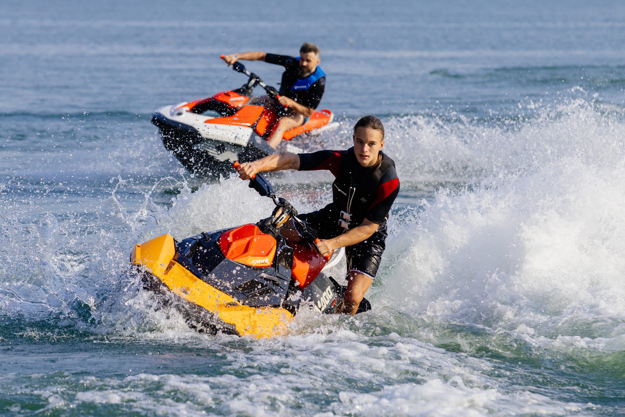Two riders carving modern jet skis with spray
