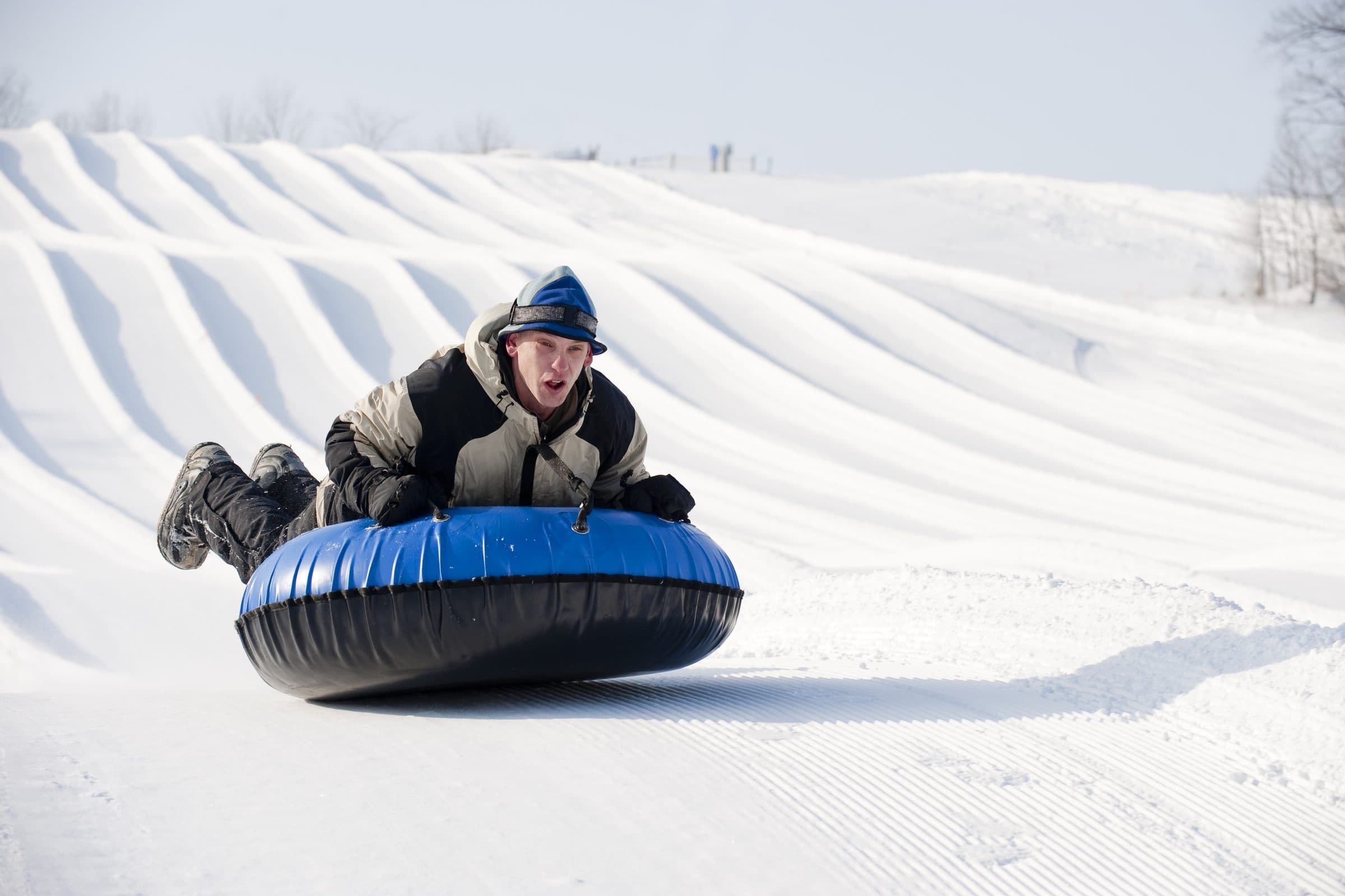 Smiling rider on a blue tube sliding down a groomed snow-tubing lane