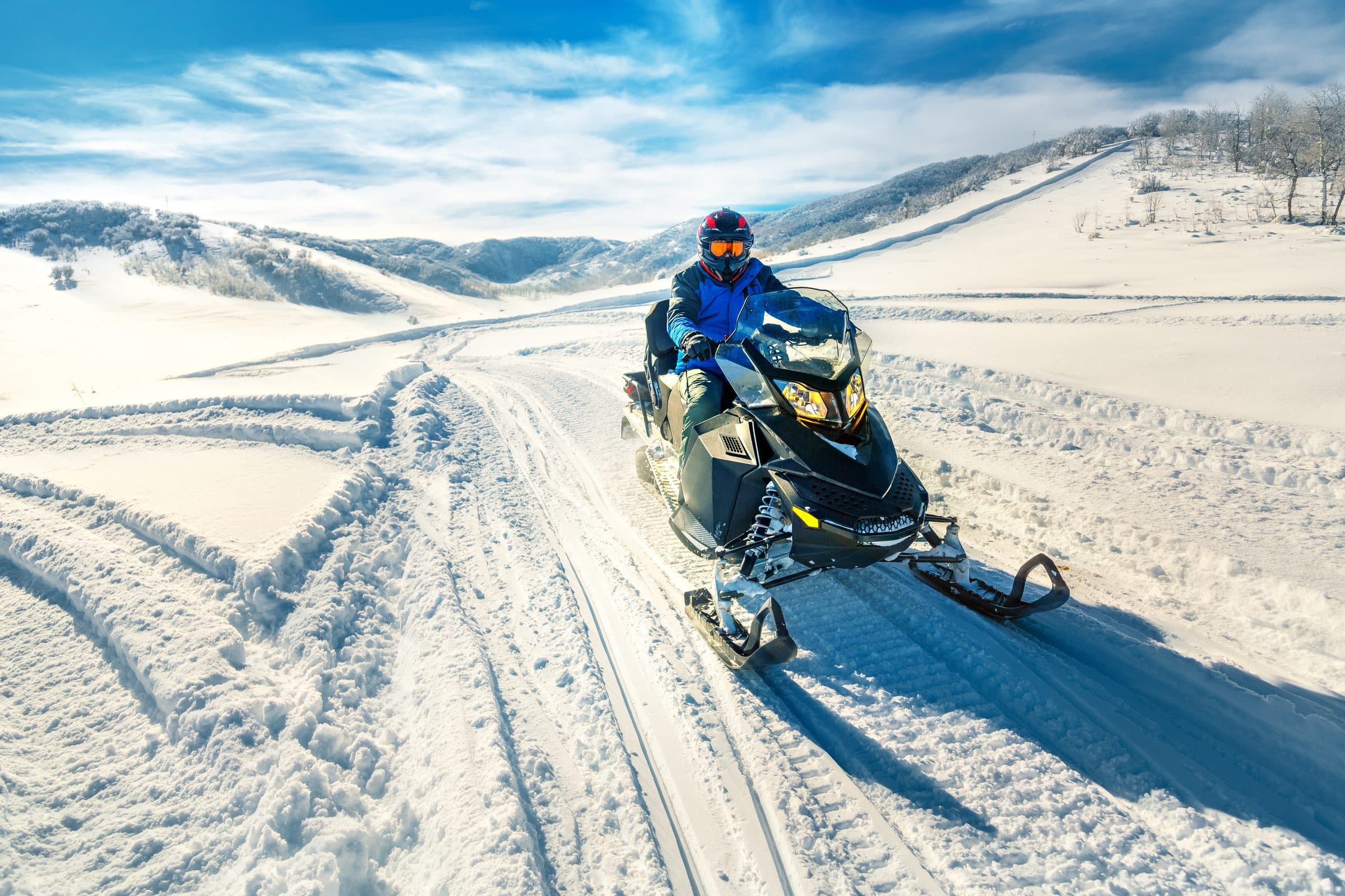 Snowmobiler riding toward camera across fresh tracks in bright sun