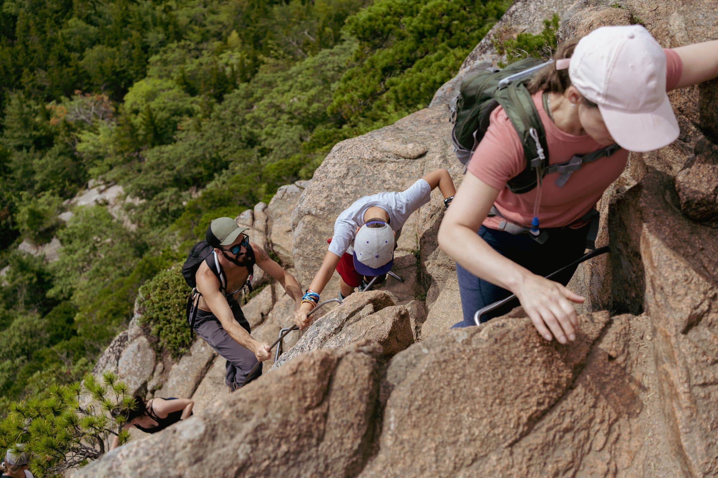 Climbers clipped in on a via ferrata rock face above a green valley