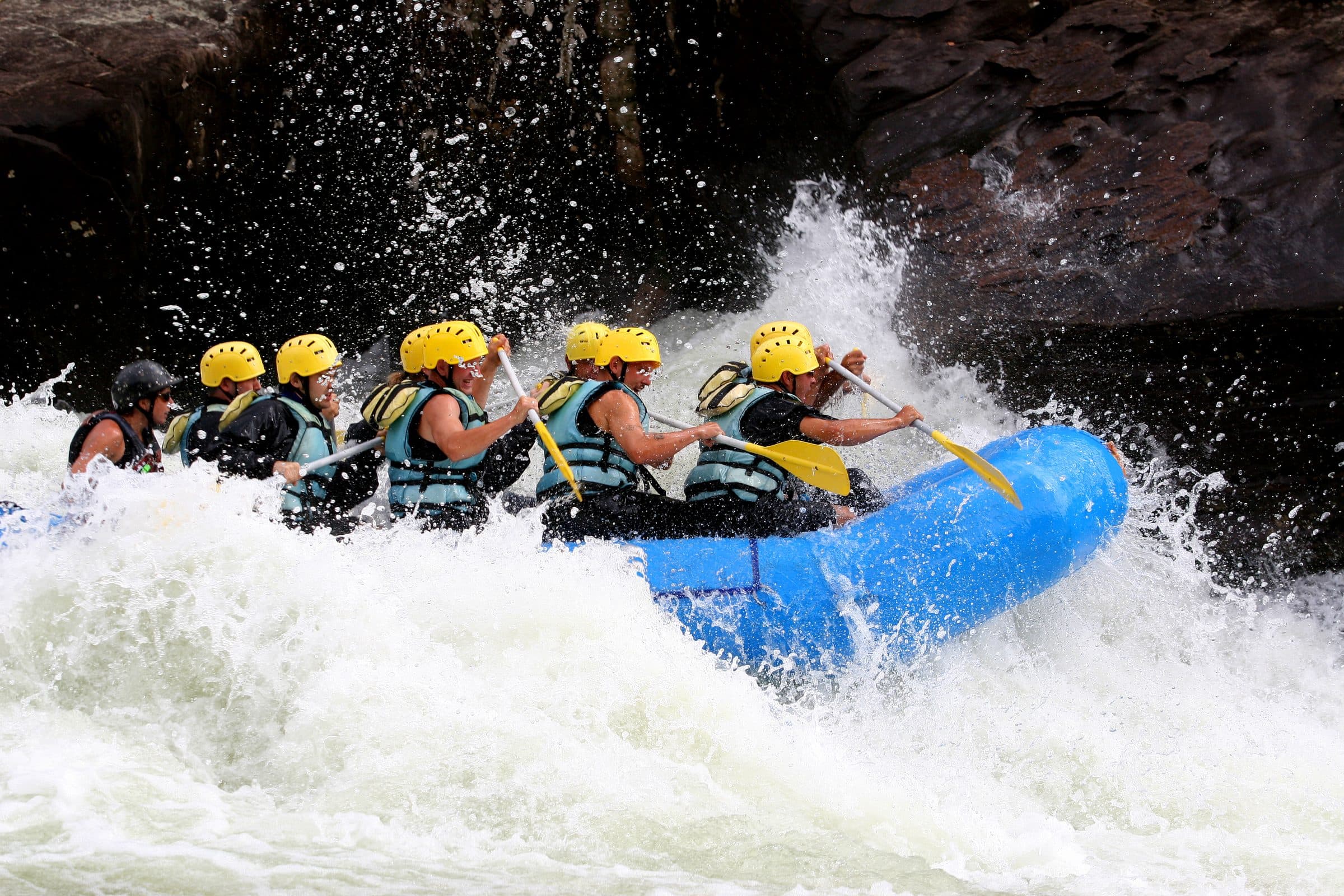 Raft crew in yellow helmets punching a big white rapid against dark rock