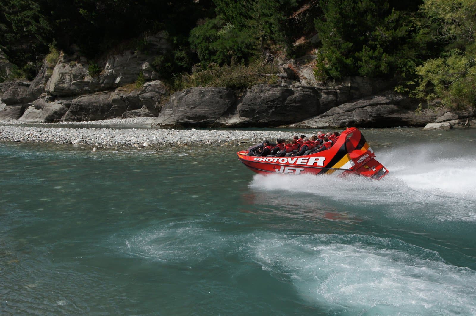 A red jet boat turning hard on a river and kicking up spray