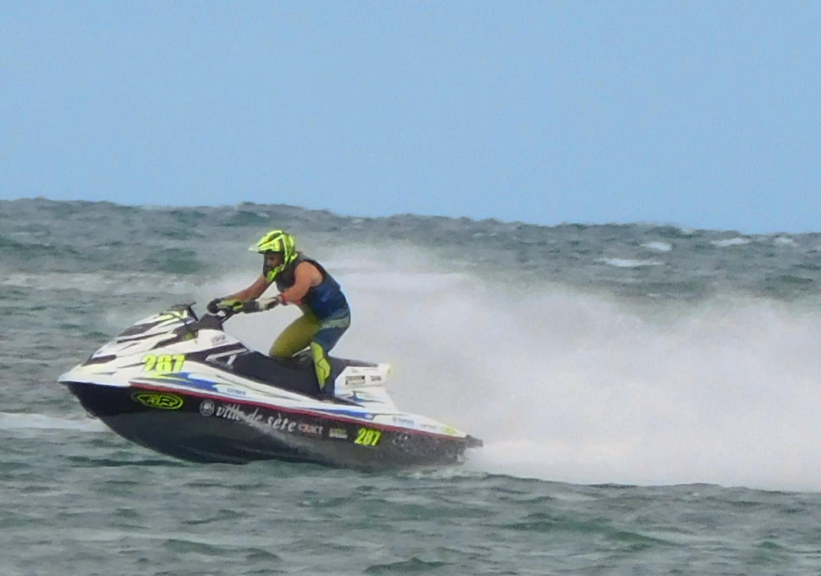 A rider on a racing jet ski throwing spray across the water