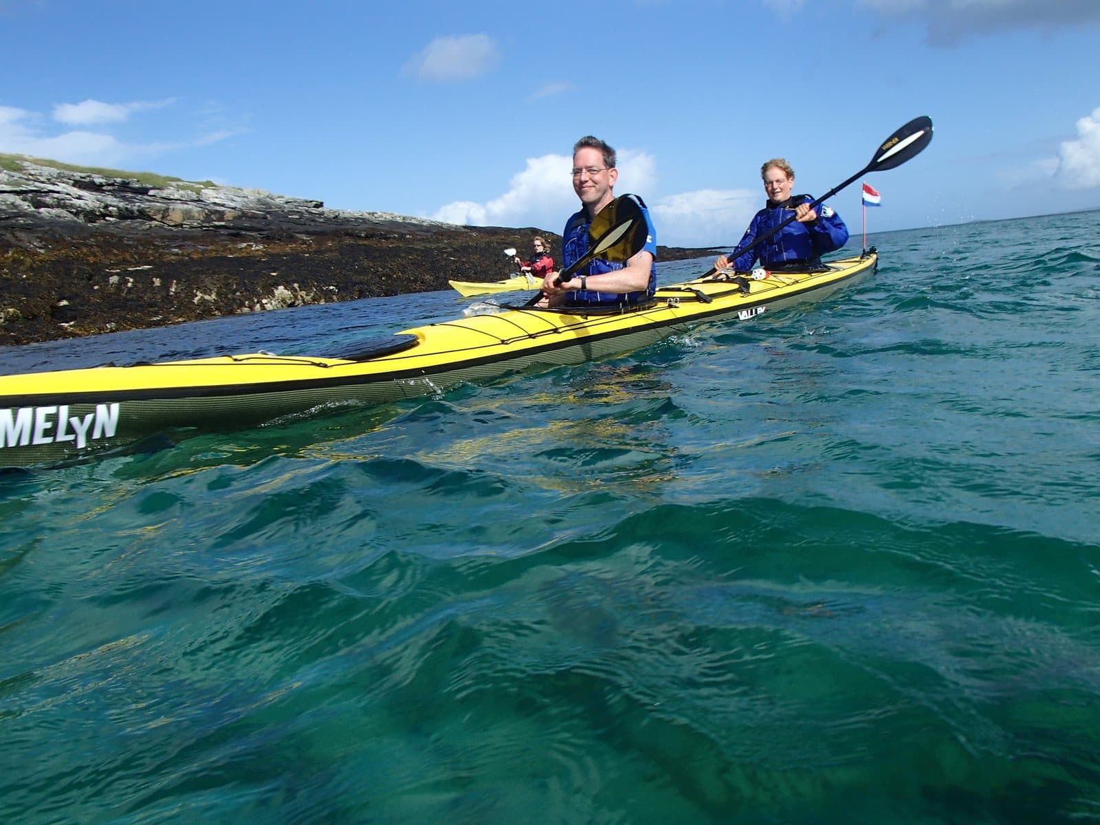 Two paddlers in a yellow double sea kayak on clear green water