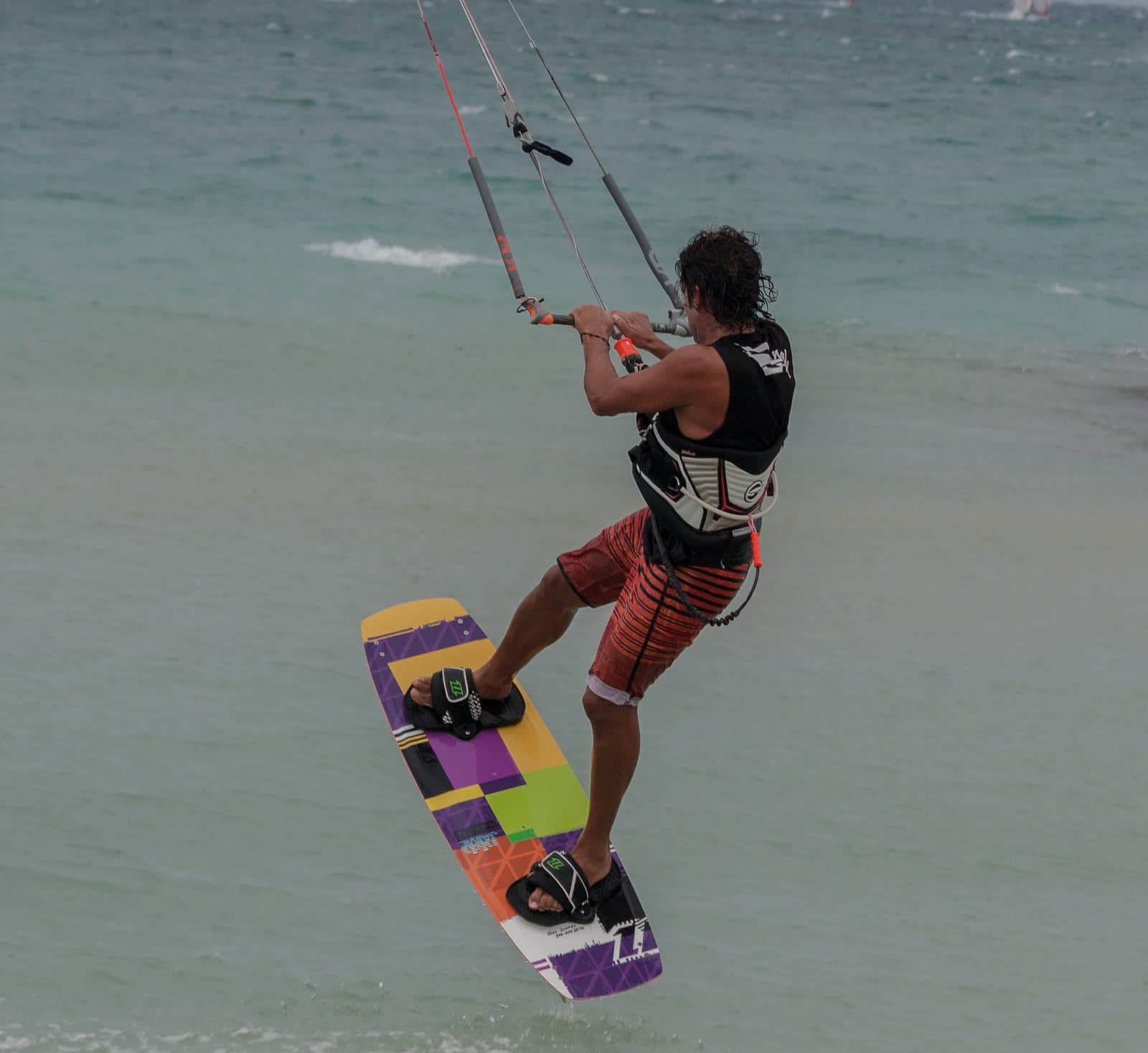A kiteboarder in the air holding the bar with the board under his feet