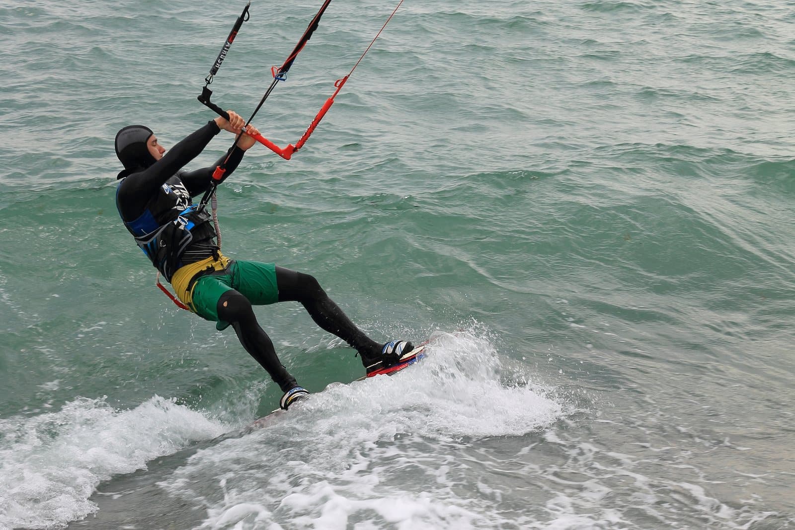 A kitesurfer holding the control bar while riding through choppy water