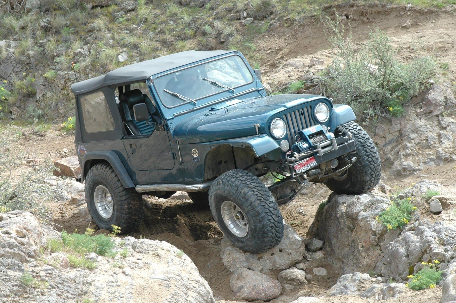 A Jeep climbing over a steep rocky obstacle with one tire lifted