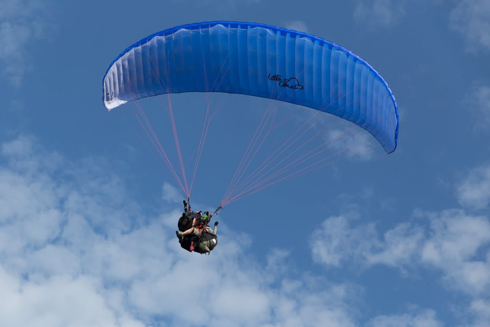 A tandem paraglider under a blue wing flying among white clouds