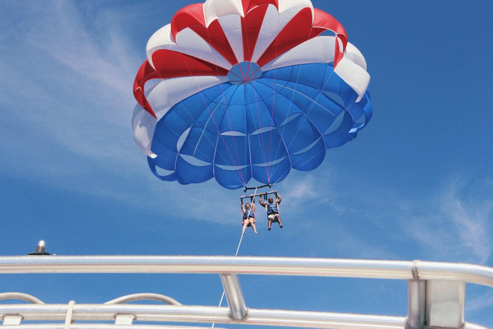 Two people parasailing under a red, white and blue canopy, towed behind a boat