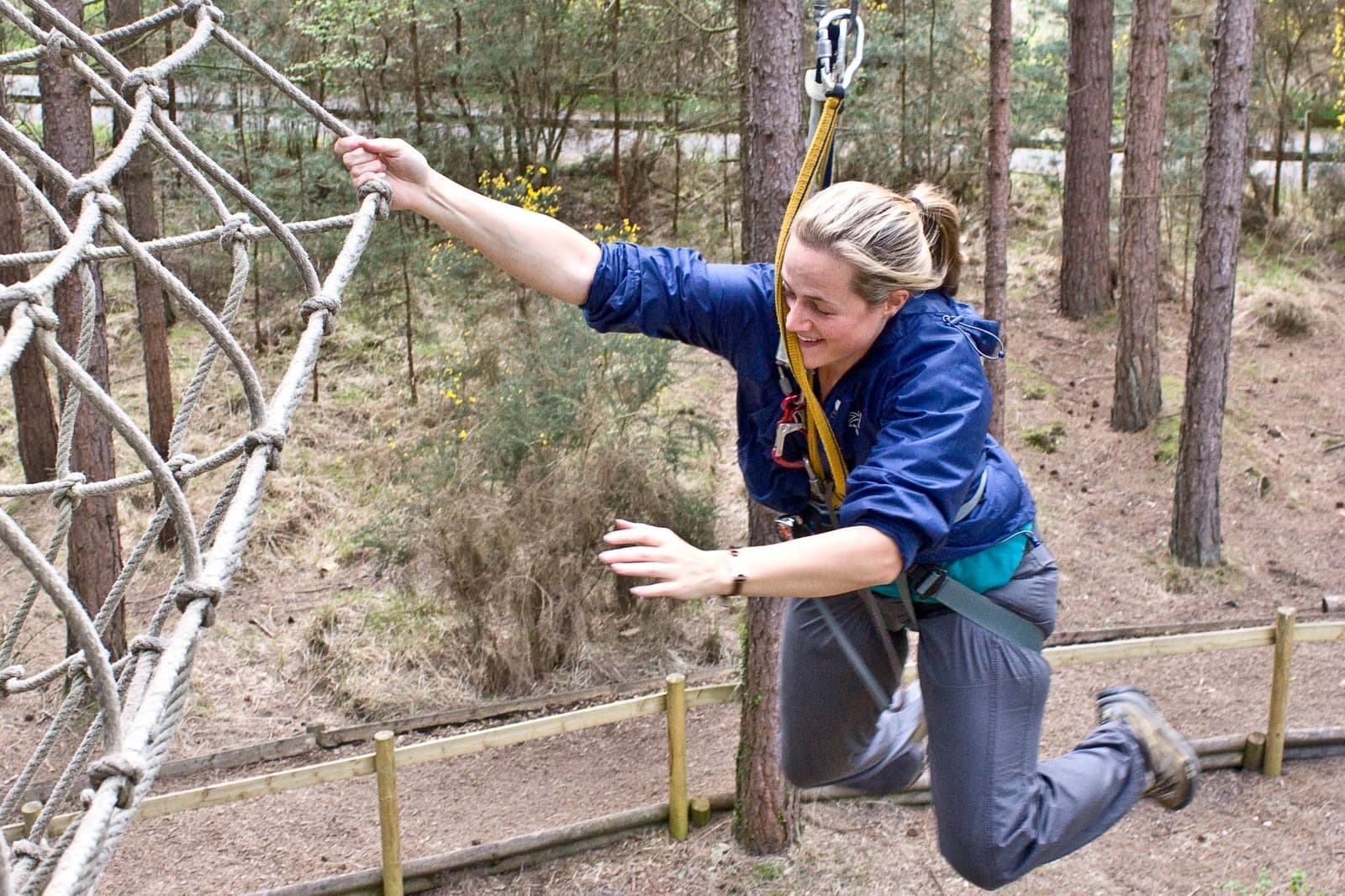 A person in a harness lunging off a cargo net on a treetop ropes course
