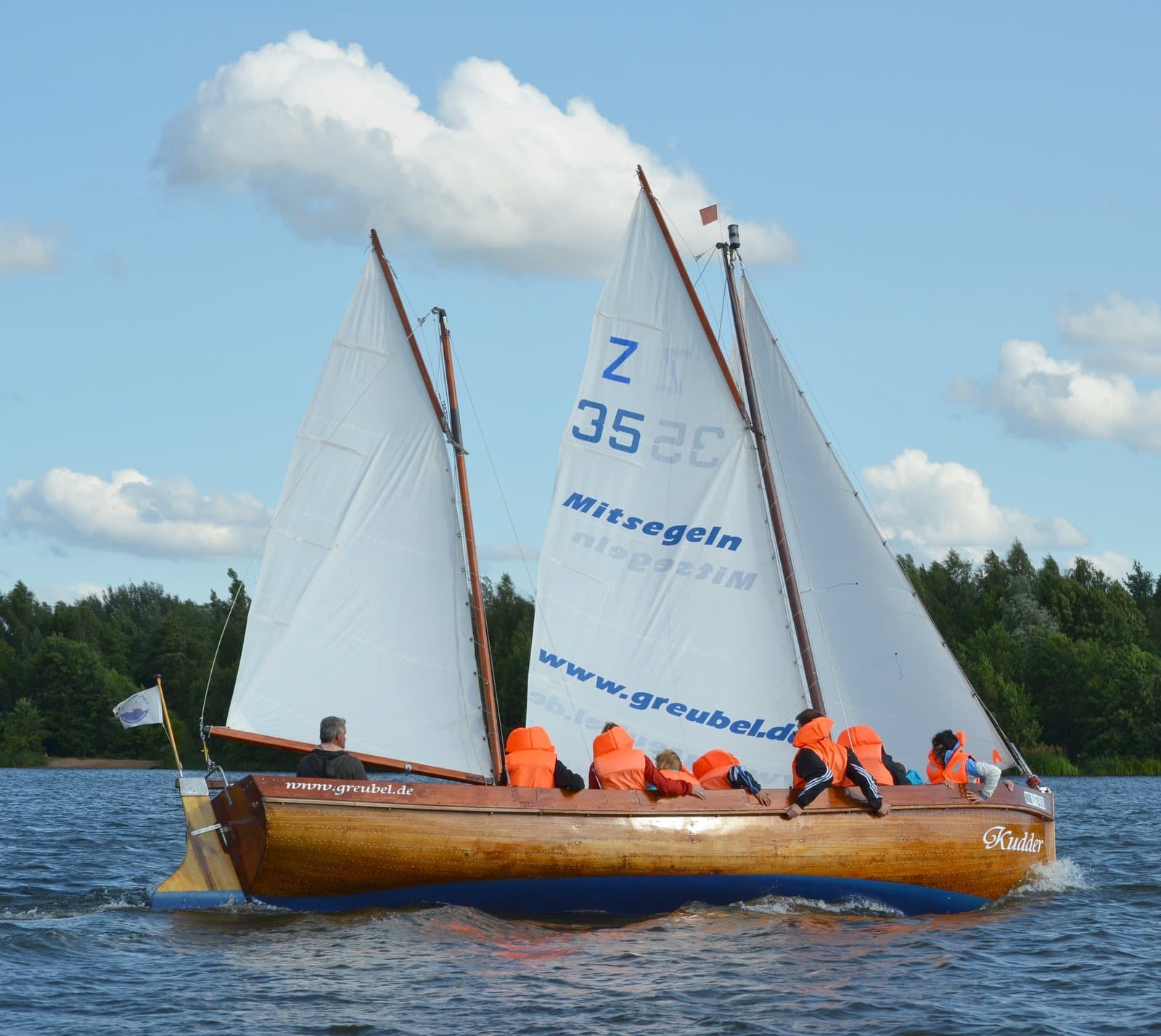 A wooden sailing boat with orange-vested students under two white sails