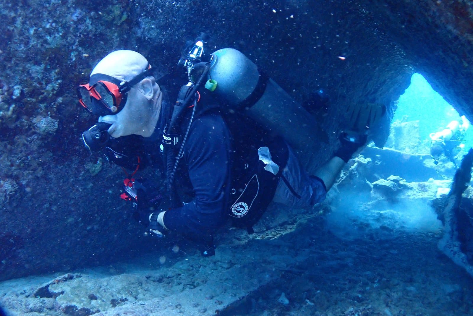 Two scuba divers in a rocky underwater cave lit by blue light