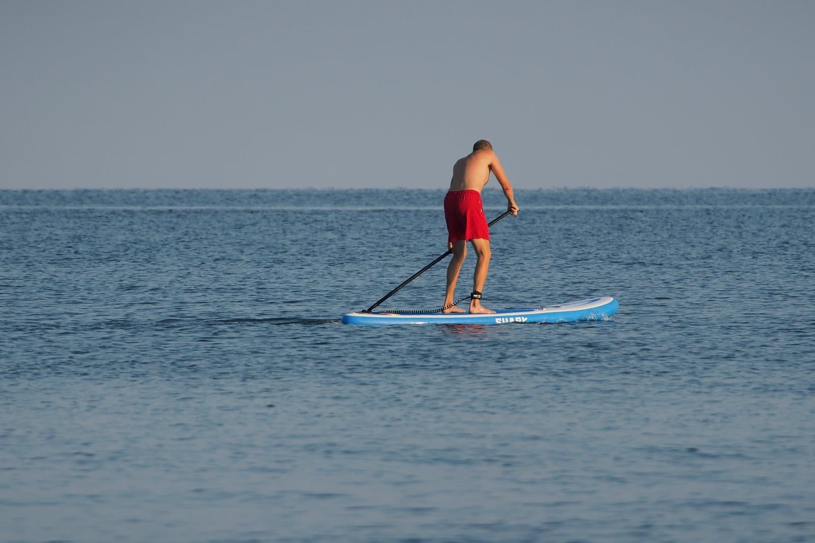 A stand-up paddleboarder paddling on calm open water