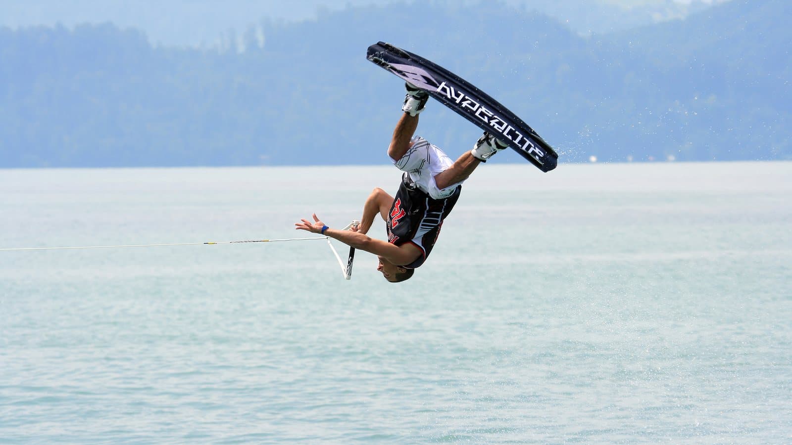 A wakeboarder upside down in the air with the board overhead