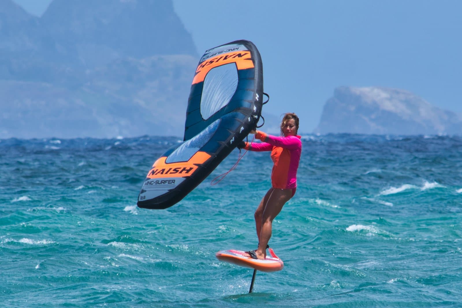 A wing foiler holding an inflatable wing while riding a foil board above the water