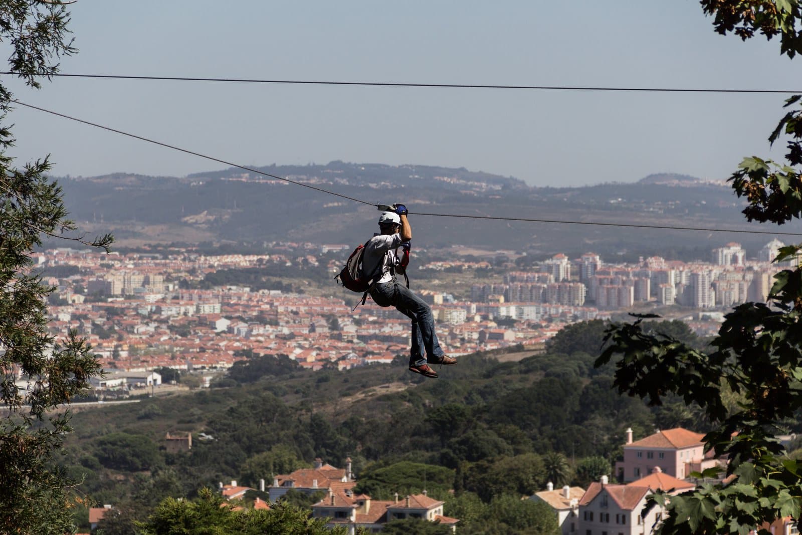 A rider in a harness flying along a zipline high above a town