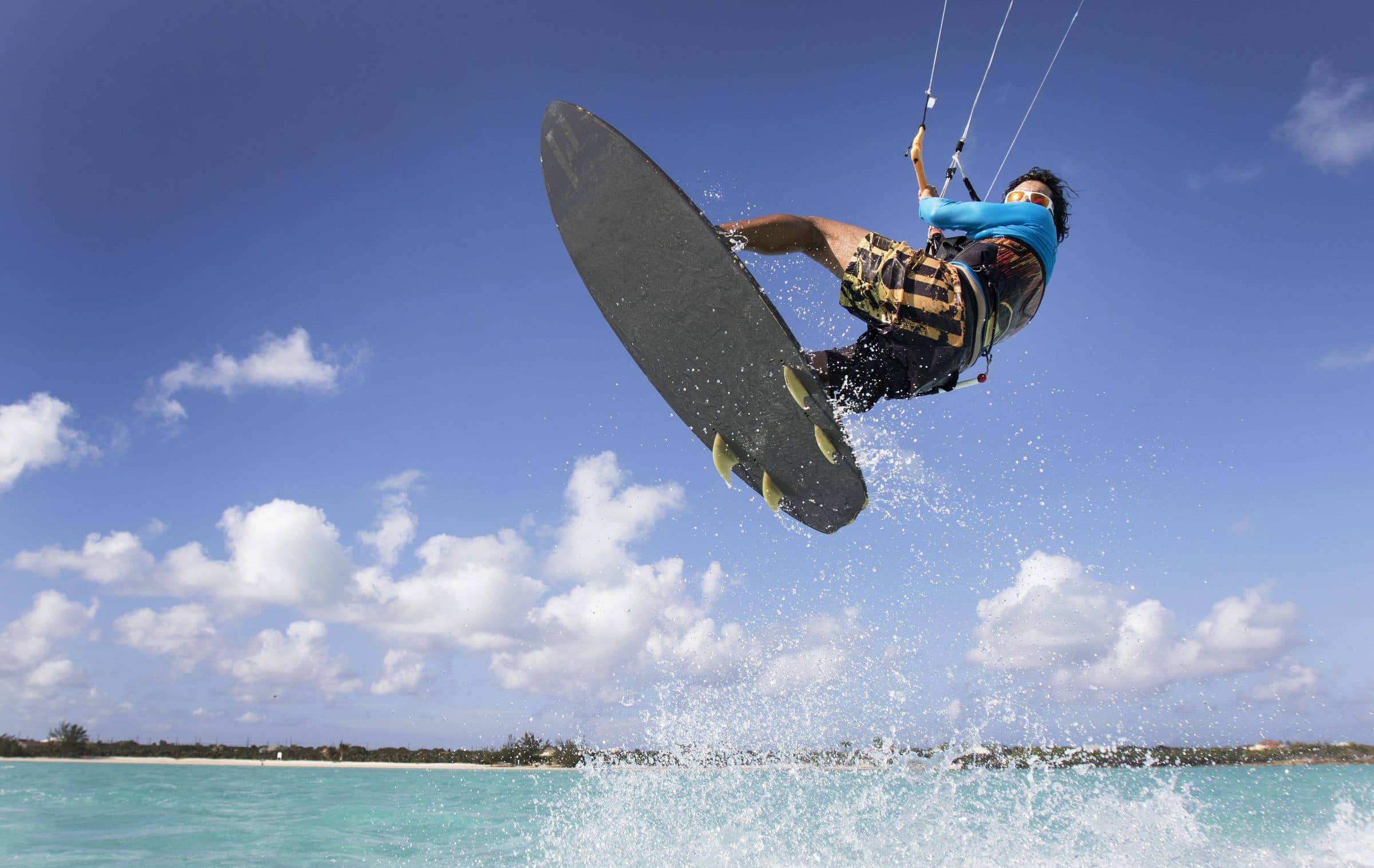 Kiteboarder high mid-jump, board big, blue sky, turquoise water